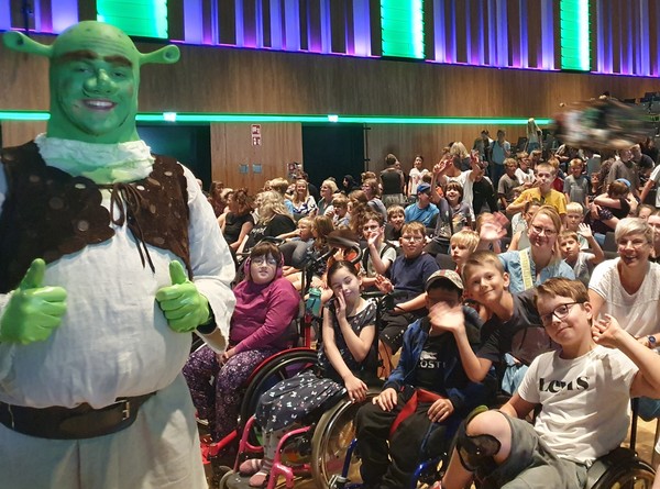 Das Foto zeigt den Darsteller Shrek und die begeisterten Zuschauer:innen der Brückenschule.