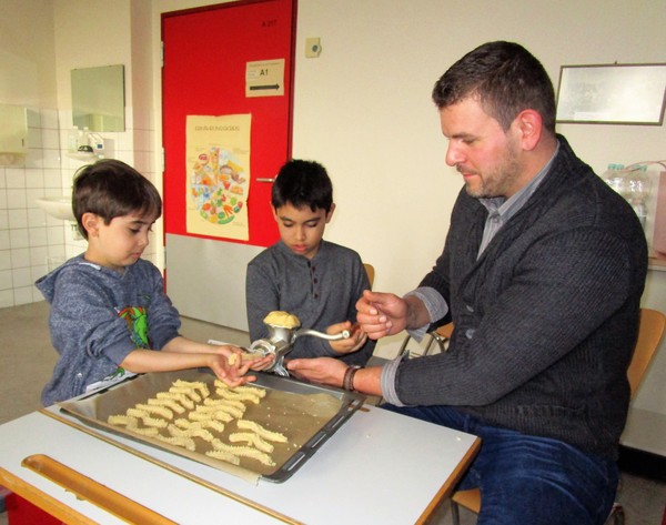 Ein Foto zeigt einen Vater und zwei Schüler beim gemeinsamen Plätzchenbacken.